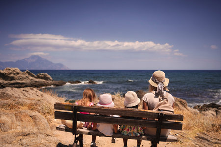 Family bonding on a sunny beach with ocean waves and distant mountainsの写真素材