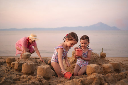 Joyful family building sandcastles on the beach at sunsetの写真素材
