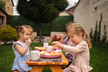 Young children enjoying a delightful outdoor meal in bright sunshineの写真素材