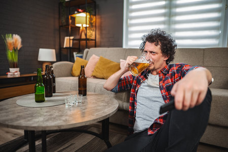Mid adult man drinking beer and watching tv at homeの写真素材