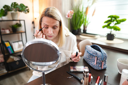Applying makeup in a cozy room with natural light and greeneryの写真素材