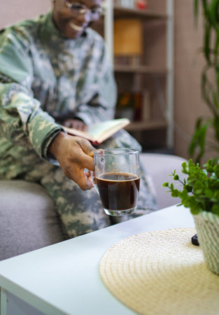 Soldier relaxing at home, reading a book and drinking coffeeの写真素材