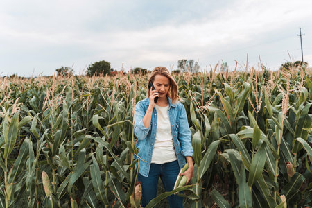 Farmer woman talking on phone and inspecting corn in field