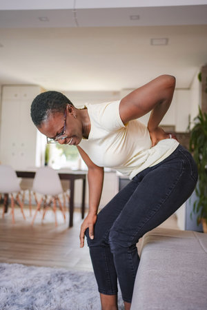 Young woman suffering from back and knee pain at home