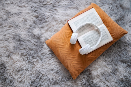 Open book and headphones resting on a cozy pillow on a soft carpet
