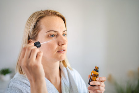 Woman applying serum on face with pipette in bathroom