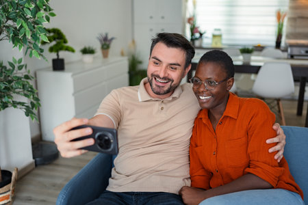 Happy multi-ethnic couple taking a selfie on the sofa at home