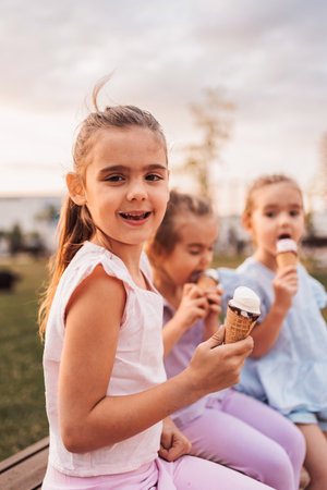 Three little girls enjoying ice cream cones in a park