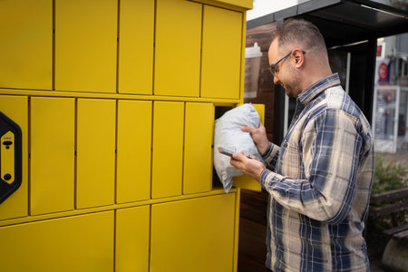 Man retrieving a package from a yellow delivery locker in a busy urban area during daylight hours