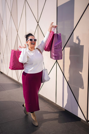 Joyful shopper showcases colorful bags against modern backdrop