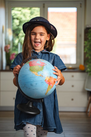 Cute little girl holding a globe, learning geography at home