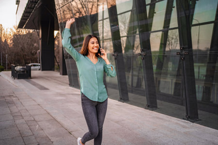 Young businesswoman celebrating success on the phone outside modern office buildingの写真素材
