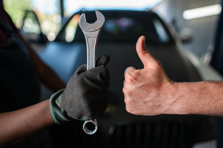 Mechanics holding wrench and making thumbs up sign in auto repair shopの写真素材