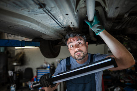 Mechanic inspecting car chassis using led work light in garageの写真素材