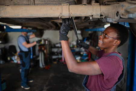 Young african female mechanic repairing car in auto repair shopの写真素材