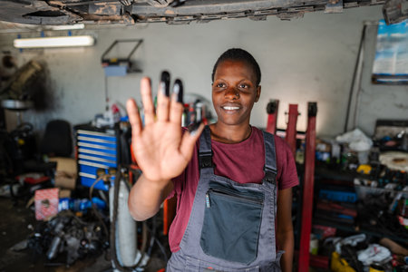 Young African Female Mechanic Showing Stop Sign with Dirty Hand in Garageの写真素材