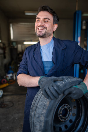 Mechanic holding a tire and smiling in a garageの写真素材