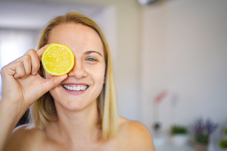 Smiling woman holding lemon slice over eye promoting healthy lifestyleの写真素材