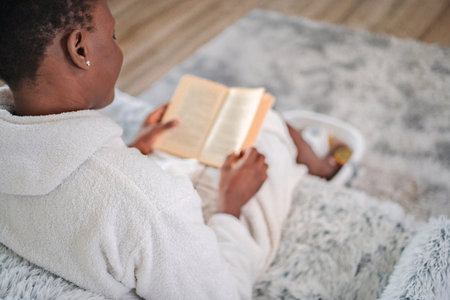 Young woman relaxing at home, reading a book and enjoying a foot bathの写真素材