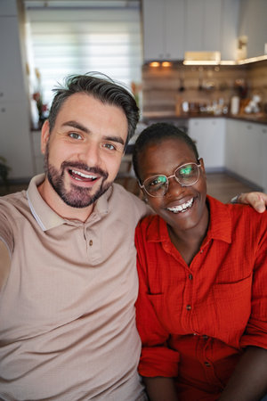 Young multi-ethnic couple taking a selfie while sitting on the sofa at homeの写真素材