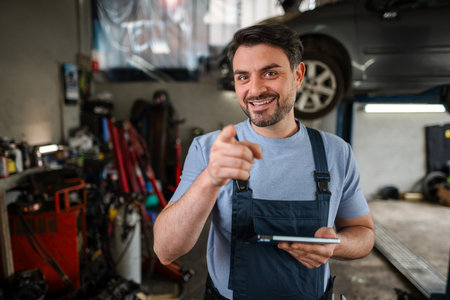 Mechanic pointing with finger and holding tablet in auto repair shopの写真素材