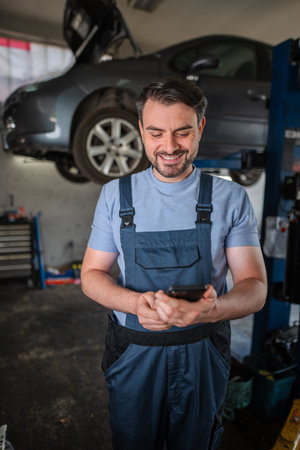 Happy mechanic using mobile phone in a car repair shopの写真素材