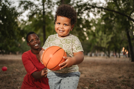 Happy toddler playing basketball with his mother in a parkの写真素材