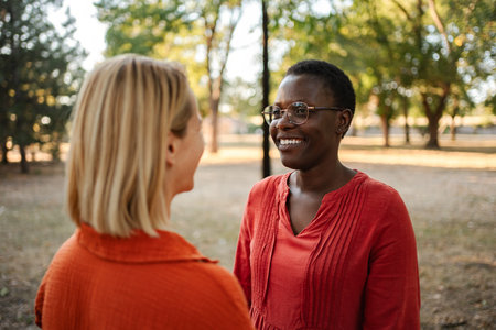 Two young women smiling and talking in a parkの写真素材