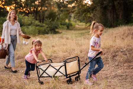 Mother and daughters pulling a cart, enjoying a picnic in the woodsの写真素材