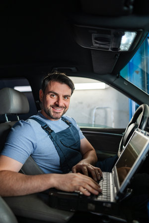 Smiling car mechanic using laptop for diagnostics inside a carの写真素材
