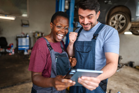 Two happy mechanics cheering while looking at a digital tablet in a garageの写真素材