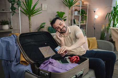 Man packing suitcase and talking on phone before travelingの写真素材