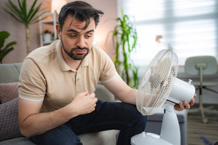 Man refreshing himself with a fan during a heat wave at home