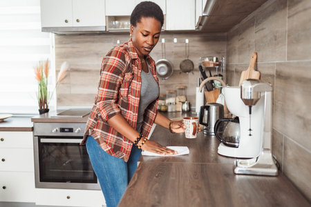 Young Woman Cleaning Kitchen Counter While Holding Coffee Cupの写真素材