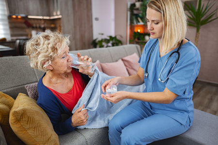 Caring nurse assists elderly woman with medication in cozy living roomの写真素材