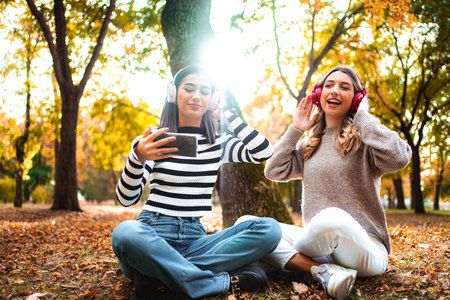 Friends enjoying autumn vibes while listening to music in the park during sunset
