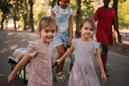 Children pulling cart with blanket in park with babysitters