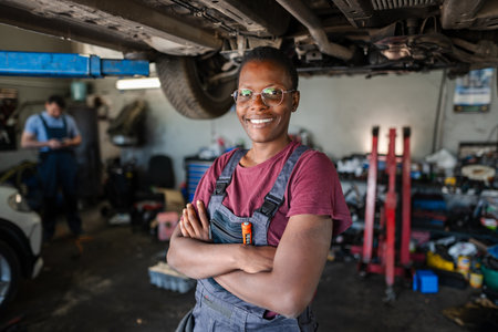 Confident Female Mechanic Smiling with Arms Crossed in Auto Repair Shopの写真素材