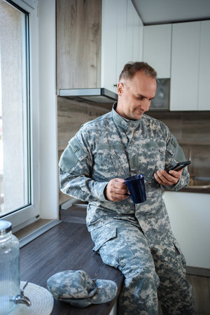 Soldier enjoying a coffee break and checking his phone in the kitchen