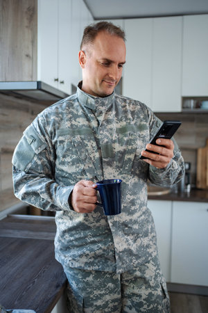 Soldier enjoying a coffee break and checking his phone in the kitchen