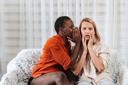 Woman telling surprising news to her friend at homeの写真素材