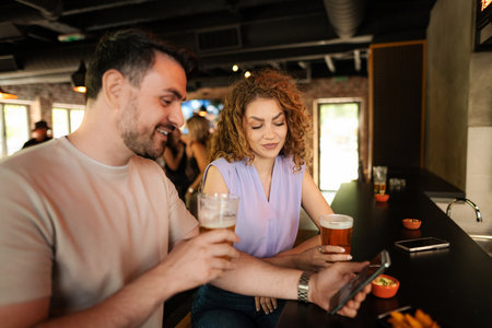 Couple enjoying drinks and using smartphone in pubの写真素材