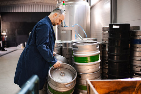 Brewery worker stacking empty beer kegs in warehouseの写真素材