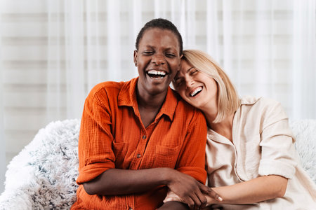 Two joyful friends laughing and embracing on a sofaの写真素材