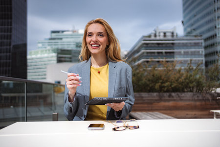 Young businesswoman smiling, working outdoors with tablet in cityの写真素材