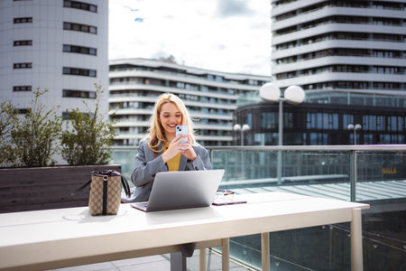 Young businesswoman using smartphone and laptop for remote workの写真素材