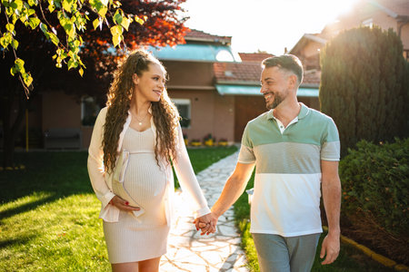 Expecting parents stroll together in evening sunlightの写真素材
