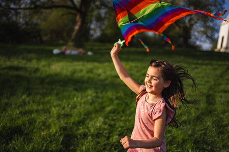 Joyful girl flying a vibrant kite on a sunny afternoon in springの写真素材