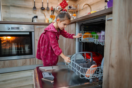 Little helper organizes dishes in the kitchen while enjoying a cozy family moment during the eveningの写真素材