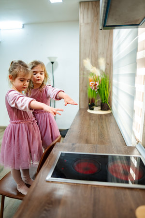 Two curious girls exploring a modern kitchen with interactive cooking technology during a bright afternoon playtimeの写真素材